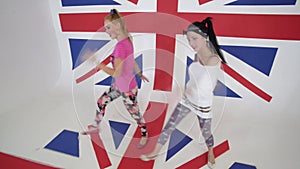 Two female dancers look at camera and move in white studio with big UK flag