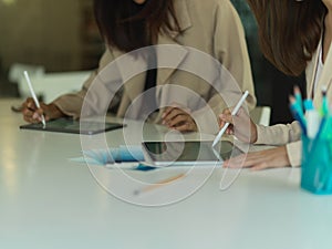 Two female designers working on digital tablet and supplies in meeting room