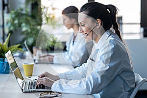 Two female doctor making video call with laptop while talking with earphone sitting in the consultation photo