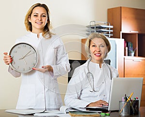 Two female doctors holding clock