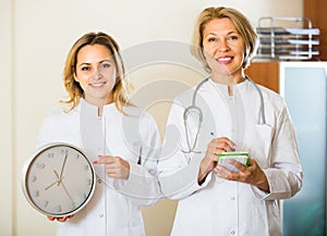 Two female doctors holding clock