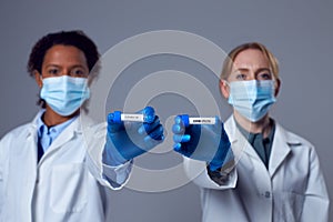 Two Female Doctors In Lab Coats Holding Test Tubes Labelled Omicron And Covid-19