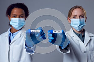 Two Female Doctors In Lab Coats Holding Test Tubes Labelled Vaccine And Omicron