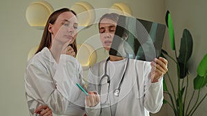Two female doctors look at the patient's X-ray in the clinic.