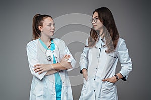 Two female doctors looking each other against grey background