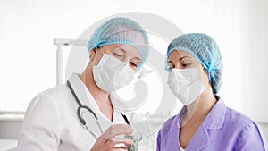 Two female doctors in medical masks discussing new treatment at hospital room. Holding bottle of pills