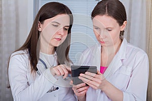 Two female doctors or nurses look at the tablet and discuss therapy