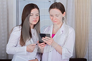 Two female doctors or nurses look at the tablet and discuss therapy