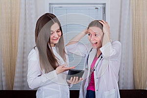 Two female doctors or nurses look at the tablet, one is shocked or very surprised