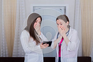 Two female doctors or nurses look at the tablet, one is shocked or very surprised