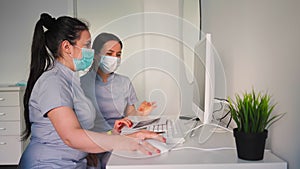 Two female doctors in protective masks discussing treatment plan sitting near computer in medical office. Healthcare and medicine