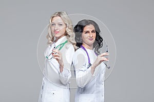 Two female doctors standing back-to-back hold ready-to-inject syringes