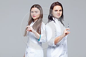 Two female doctors standing back-to-back hold ready-to-inject syringes