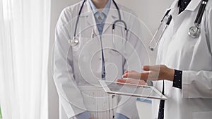 Two female doctors are using a tablet computer while standing and discussing health treatment in a hospital. Medicine