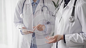 Two female doctors are using a tablet computer while standing and discussing health treatment in a hospital. Medicine