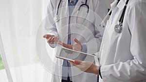 Two female doctors are using a tablet computer while standing and discussing health treatment in a hospital. Medicine