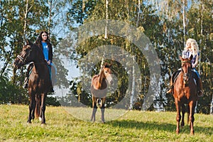 Two female equestrians with purebred brown horses and foal between them.