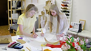 Two female fashion designers working together at workplace at workshop for sewing clothes, brainstorming over new dress