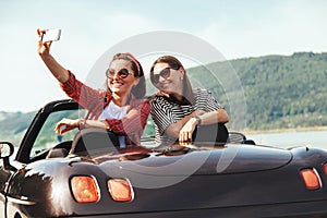 Two female freinds take selfie photo in cabriolet car with beaut