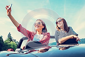 Two female freinds take a selfie photo in cabriolet car during t