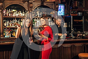 Two female friends are in the bar for a drink and talk. The woman with talks near the ear of the friend