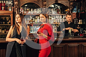 Two female friends are in the bar for a drink and talk. The woman with talks near the ear of the friend