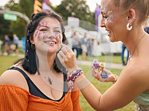 Two Female Friends Decorating Faces With Glitter At Summer Music Festival 