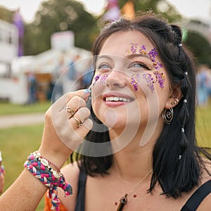 Two Female Friends Decorating Faces With Glitter At Summer Music Festival 