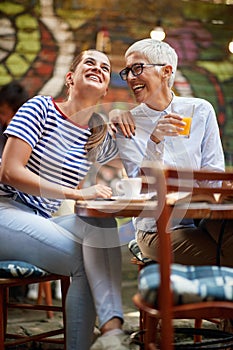 Two female friends of different generations joking while they have a drink in the bar. Leisure, bar, friendship, outdoor