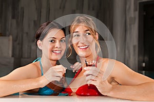 Two female friends drinking tea in swimming pool