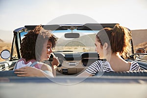 Two Female Friends Enjoying Road Trip In Open Top Classic Car