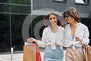 Two female friends have a shopping day. Walking outdoors with bags