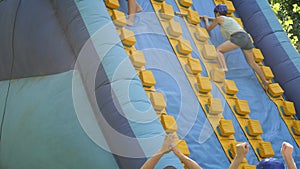 Two female friends having fun in outdoor amusement park on summer day, climbing on inflatable slide with wooden poles