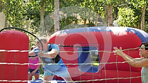 Two female friends having fun in outdoor amusement park on summer day, climbing on inflatable slide with wooden poles