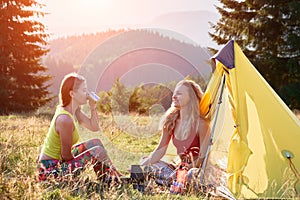 Two female friends hiking, having break in campsite.