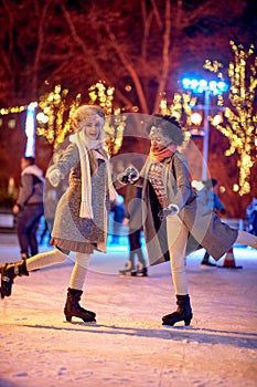 Two female friends are posing for a photo while skating at ice-skating rink during Christmas holidays in the city. Christmas, New