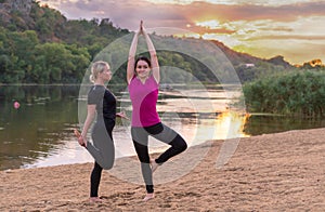 Two female friends practicing yoga on a beach