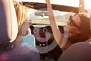 Two Female Friends On Road Trip Driving In Convertible Car