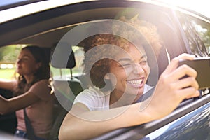 Two Female Friends Or Same Sex Couple In Car On Road Trip Vacation Taking Picture On Mobile Phone