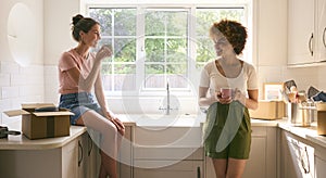 Two Female Friends Or Same Sex Couple Taking A Coffee Break From Unpacking On Moving Day In New Home