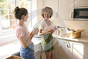 Two Female Friends Or Same Sex Couple Taking A Coffee Break From Unpacking On Moving Day In New Home