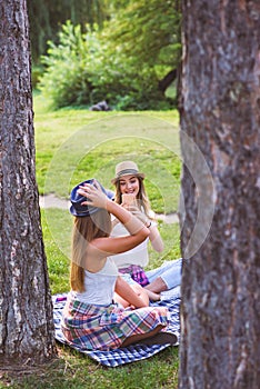 Two female friends sitting on the grass, talking and using laptop