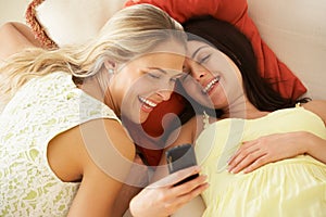 Two female Friends On Sofa Reading Text Message