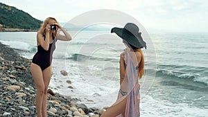 Two female friends in swimsuits taking pictures on camera on beach. Retro concept