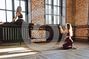 Two female friends take photo after hard workout loft style studio. Woman make picture of her flexible friend making