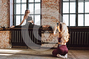 Two female friends take photo after hard workout loft style studio. Woman make picture of her flexible friend making