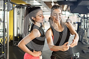 Two female friends taking a selfie photo after hard workout in gym.