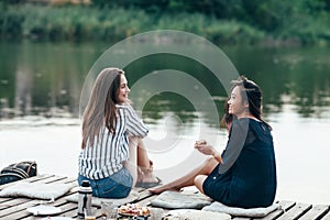 Two female friends talking at a pier relaxing on lake