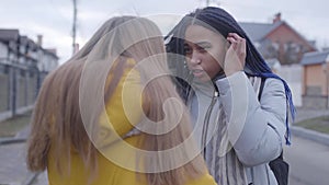 Two female friends talking, turning back to each other, African American teen leaving, Caucasian girl standing with