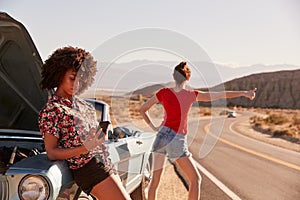 Two female friends by their broken down car at the roadside